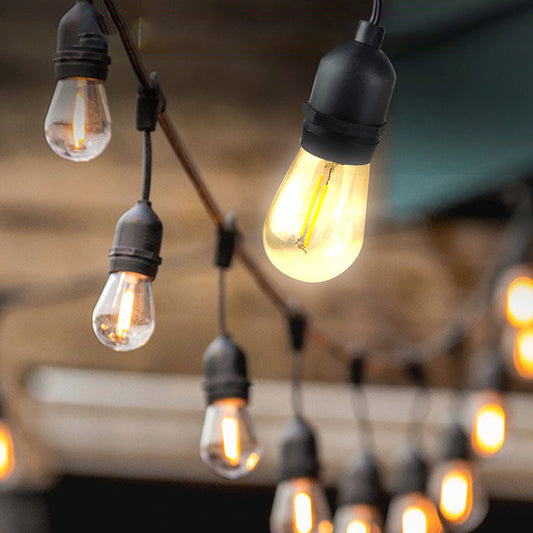 Close-up of warm glowing outdoor string lights hanging with black sockets showing how to hang outdoor string lights