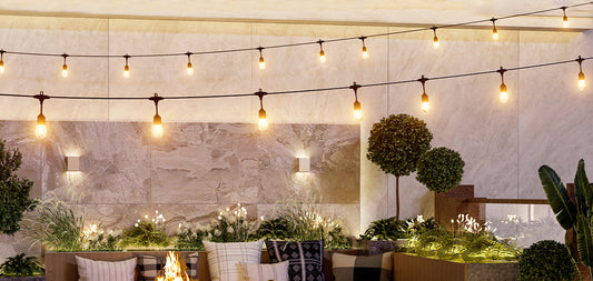 Cozy patio with string bulbs and lush plants showcasing warm garden lighting over outdoor seating