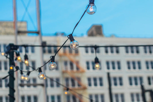 String lights hanging outdoors with a city building in the background for festive patio lighting guide