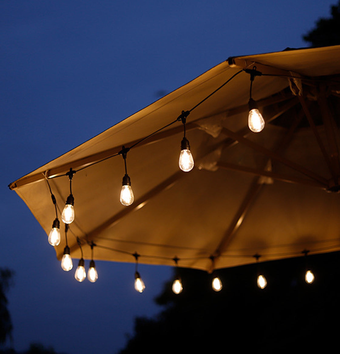 Warm glowing garden lights outdoor hanging from beige patio umbrella at dusk