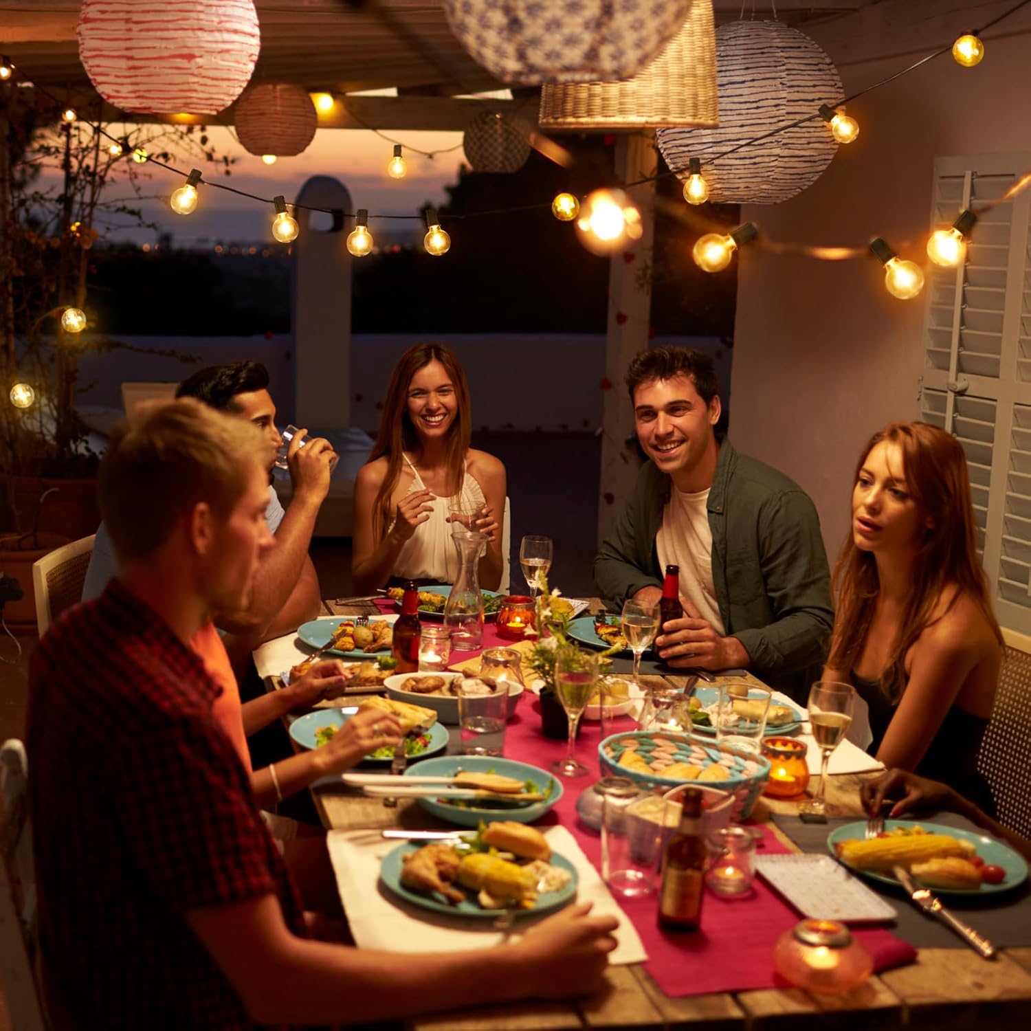Warm glowing led outdoor lights hanging above a group of friends enjoying dinner outside at night