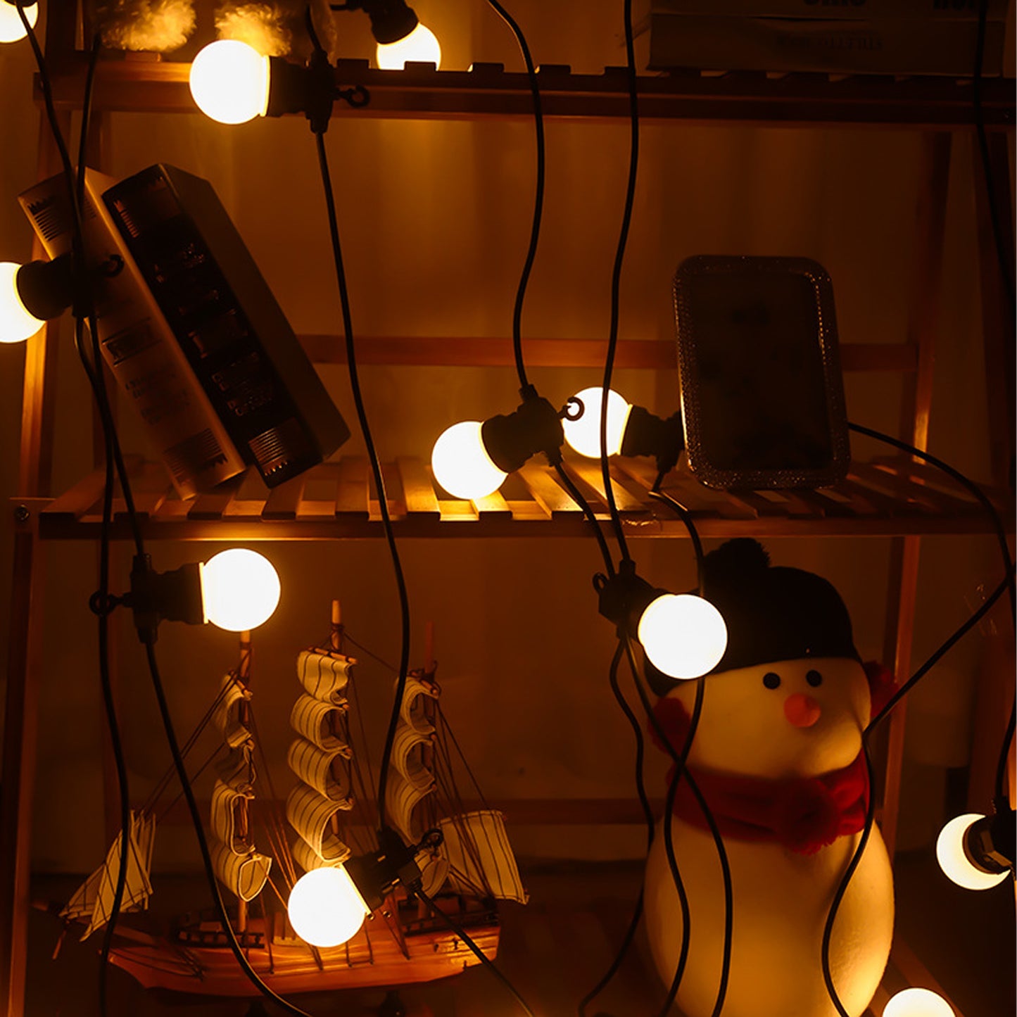 Warm white outdoor lights decoration string illuminating shelves with books, model ship, and snowman figure