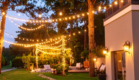 Warm glowing solar string lights outdoor decorating a backyard patio and garden area at dusk