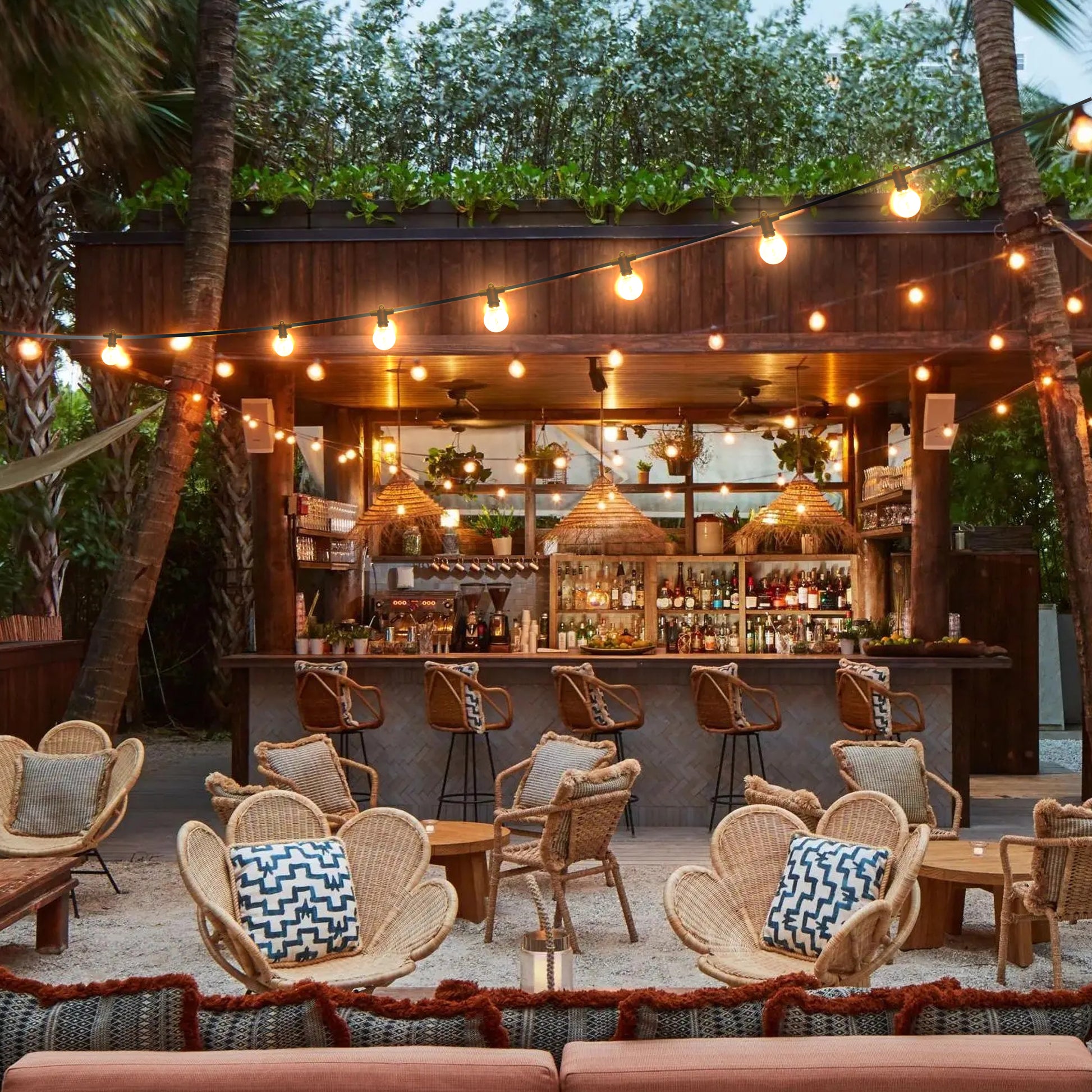 Warm glowing garden lights strung above outdoor seating area with wicker chairs and bar counter