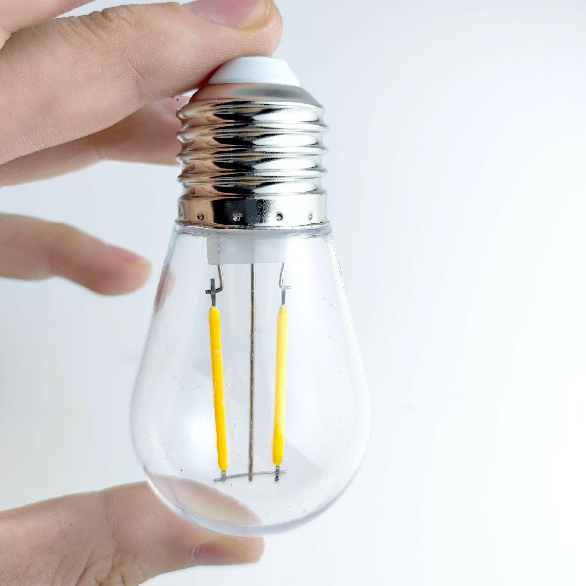 Close-up hand holding clear LED bulb for commercial waterproof string lights outdoor lighting